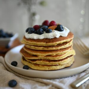 Stack of pancakes with berries and cream, perfect for breakfast indulgence.